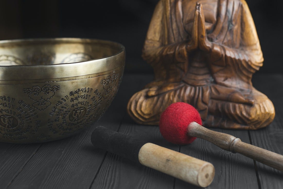 a sound bowl, praying buddha statue, and sound bowl mallet on a table