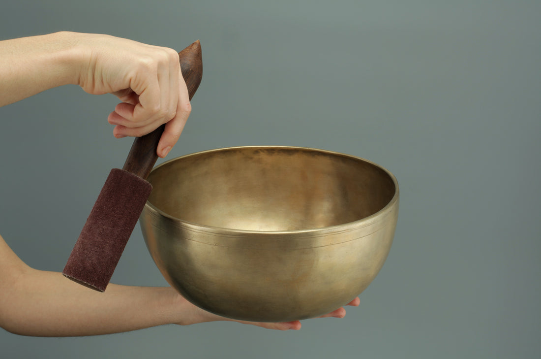 a singing bowl held in one hand being played by a mallet in the other hand